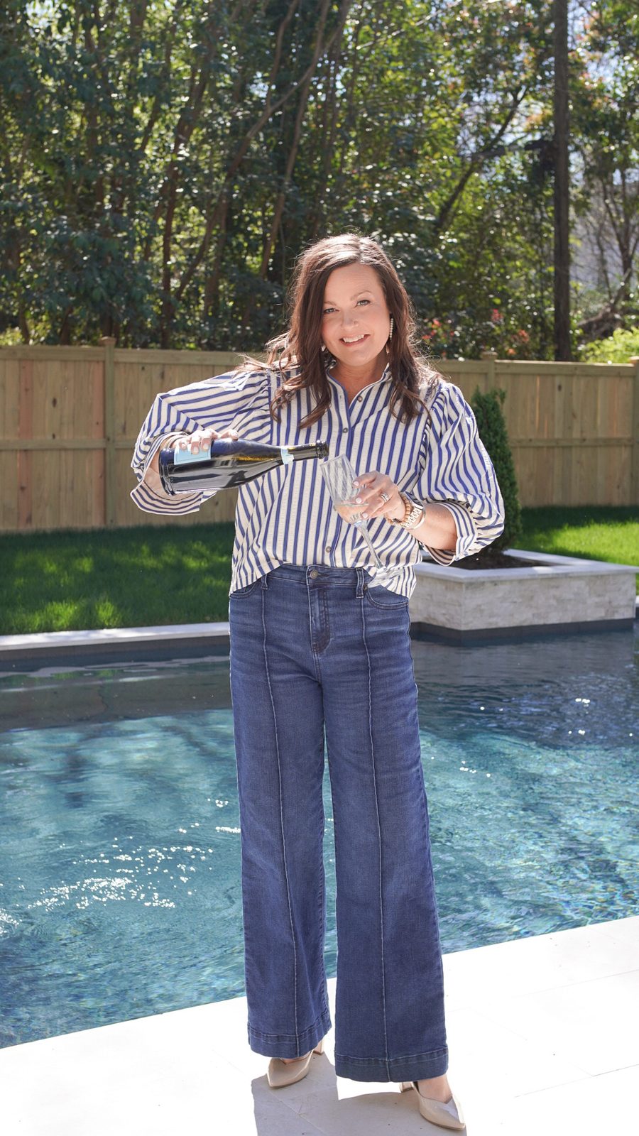 Kellee pouring a glass of wine beside a backyard pool